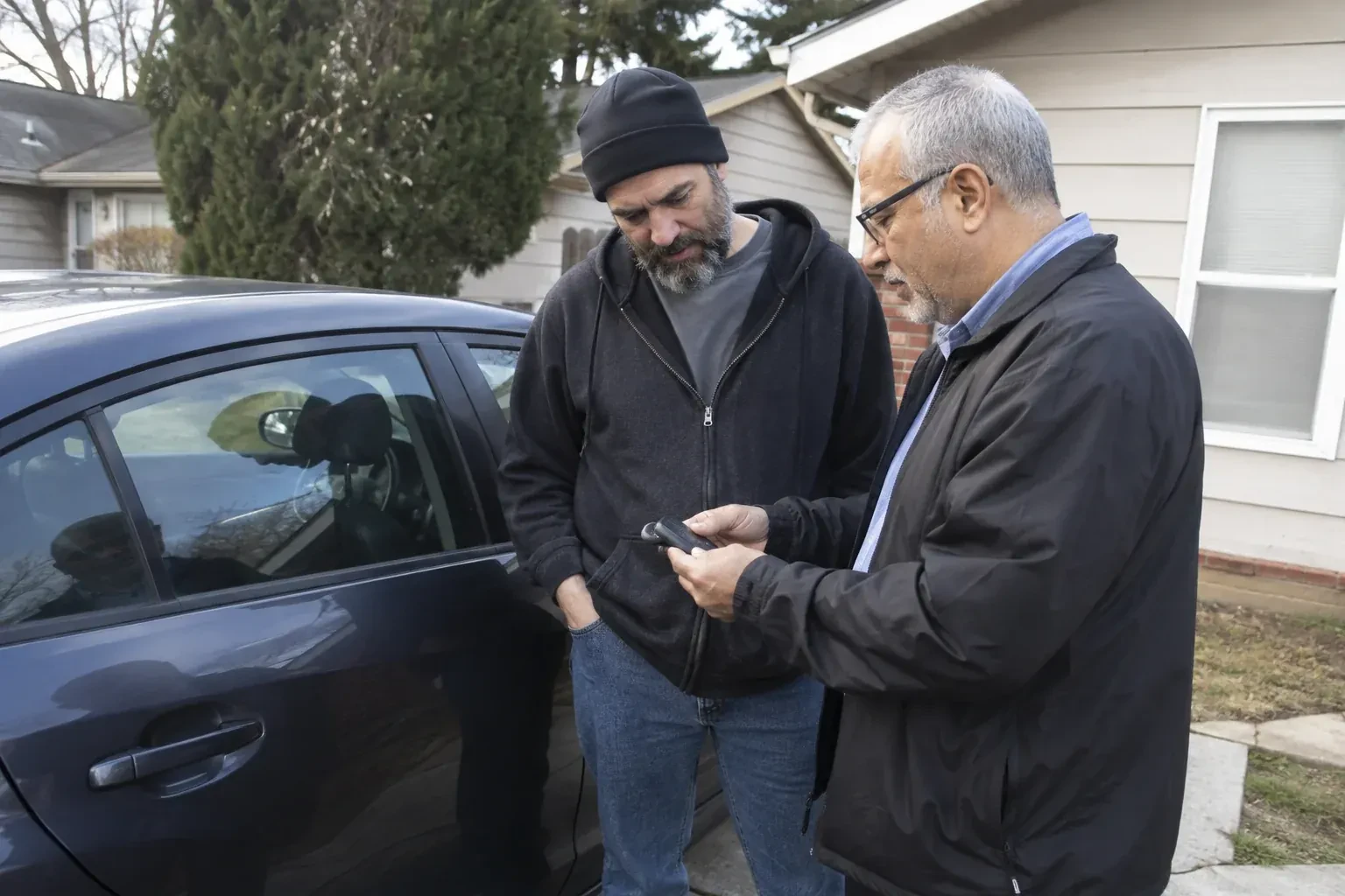 Two adults discussing a key fob beside a parked car. — Car Lockout Service, Toronto